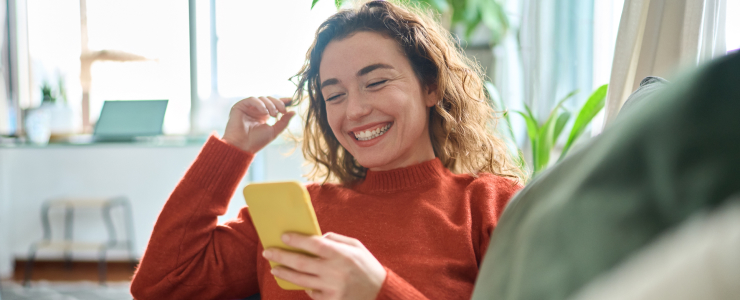 A woman smiles while holding a cell phone, conveying a sense of joy and connection.