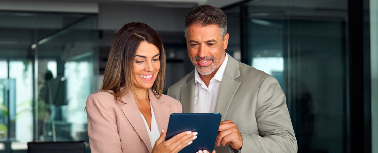 A man and woman in business attire are collaborating while looking at a tablet together.