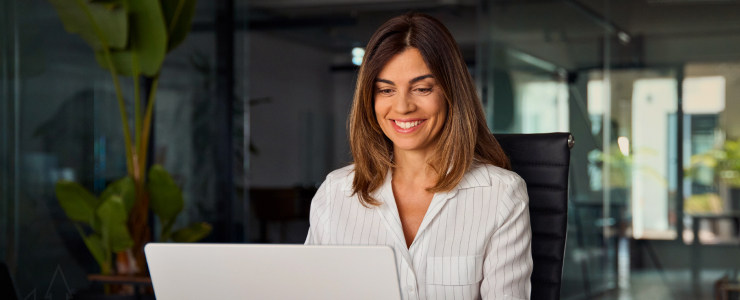 Uma mulher com uma expressão alegre, concentrada no seu computador portátil, simbolizando o sucesso no comércio forex.