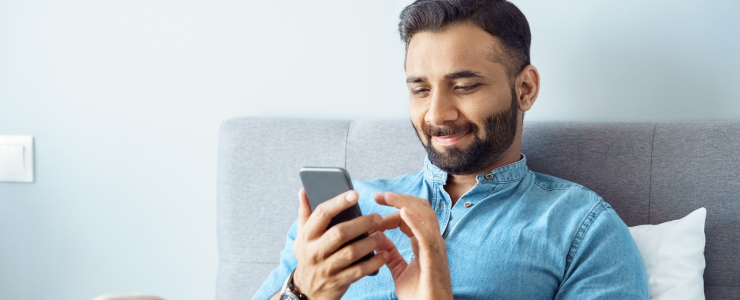 Um homem sentado numa cama, concentrado no seu telemóvel, envolvido em negociações móveis para contas forex.