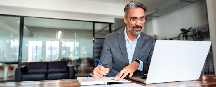 A suited man trader analyzes forex data on his laptop while seated at a desk, reflecting success in trading.