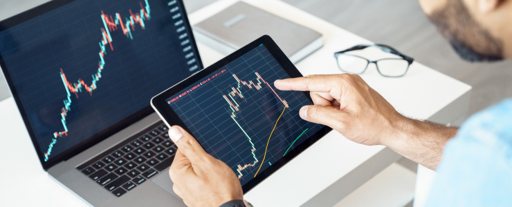 Hombre analizando gráficos bursátiles en una tableta, centrado en el comercio de divisas y las tendencias del mercado.