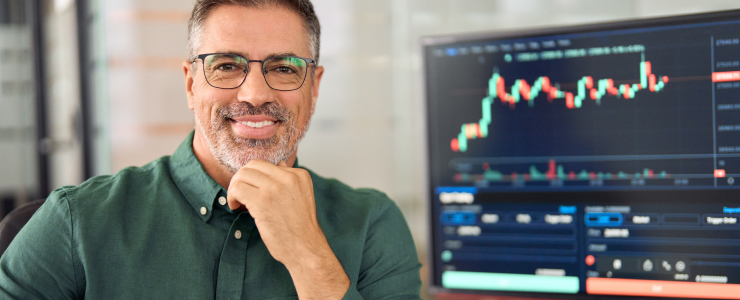 Un homme portant des lunettes sourit en regardant un écran d'ordinateur, concentré sur la plateforme de trading forex MetaTrader 4.