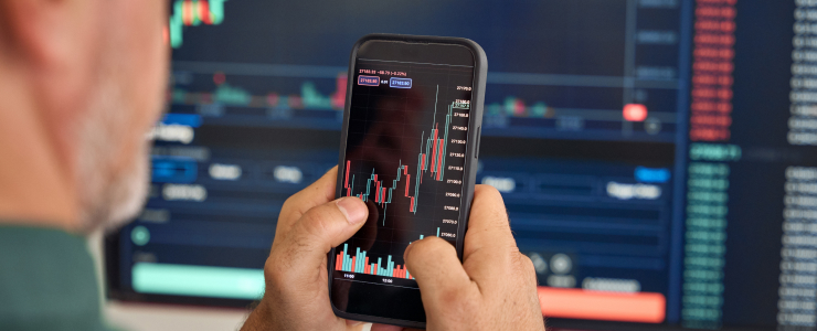A man examines a smartphone with a stock market chart, representing mobile trading analysis for forex traders.