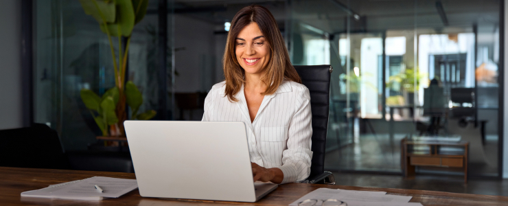 A woman focused on her laptop at a desk, engaged in commodity trading activities.
