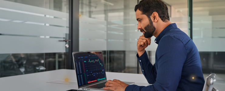 A man sitting at a desk with a laptop, actively using a trading platform for financial transactions.