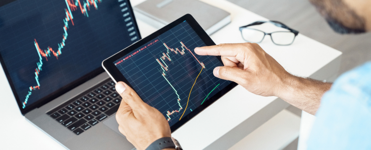 Trader using a tablet to view stock market graphs, highlighting key 5 features of a trading platform for optimal performance.